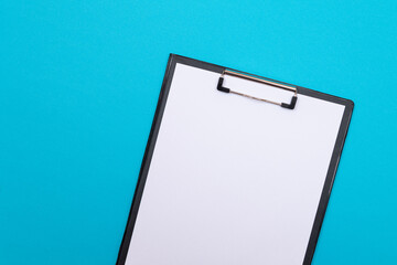 Black Clipboard with Blank White Sheet of Paper Lying on Blue Table - Top View, Flat Lay