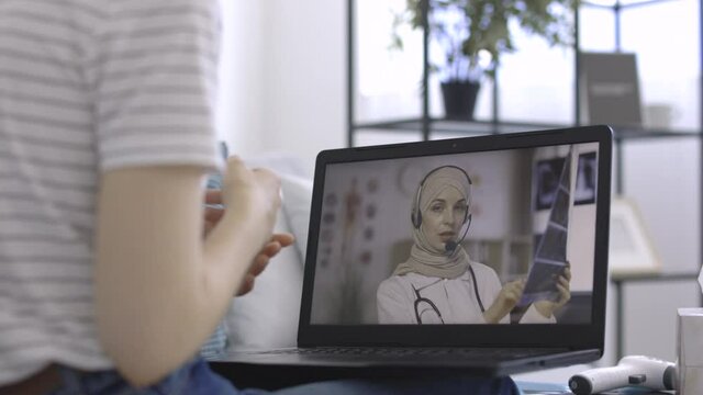 Unrecognizable female patient having video chat with Arab woman doctor on laptop pc at home, getting online consultation. Doctor explains patient's tomography. Telemedicine and remote medical services