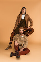 young couple in stylish autumn outfit looking at camera while posing on beige background