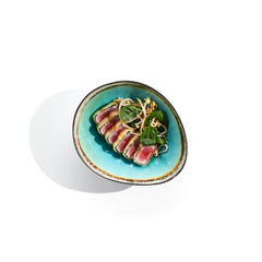 Tuna tataki - seared tuna,. thinly sliced sashimi style. Tuna tataki served with delicious citrus ponzu tataki sauce. Japanese seafood on black plate isolated on white background.