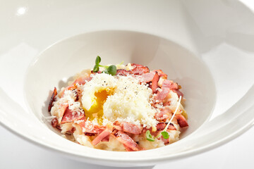 Risotto alla carbonara on white restaurant plate. Risotto with bacon and egg, garnished with micro...