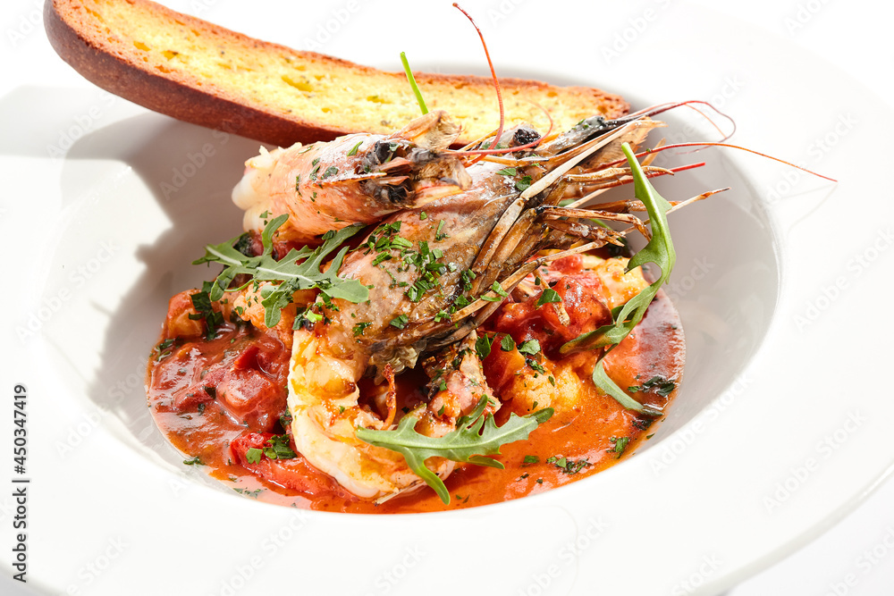 Wall mural Seafood with tomato sauce on white restaurant plate. Shrimp seafood and tomato stew garnished with fried bread. Isolated on white background.