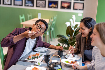 group of friends eating sushi and asian food at the japanese restaurant, multiethnic people having fun at dinner