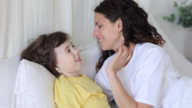 Joyful family have fun lying in bed, young caring mum blowing on kids head. Small son and female parent embracing in bedroom under blanket on eary weekend morning relaxing at home cuddling together