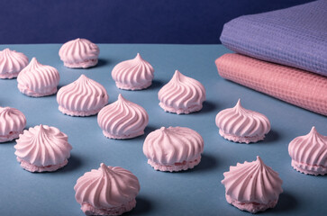 Beautifully arranged rows of delicate pink meringue cookies on a light blue background, next to cloth napkins of harmonious pink and blue colors. Light dessert.