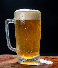 Beer mug, served cold with plenty of foam on a wooden board on a black background