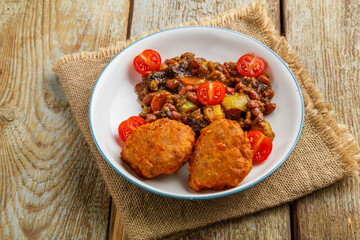 Cod cutlets with stewed potatoes and vegetables on a plate on a napkin.