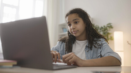 Afro-american teen girl doing homework online, looking at screen skeptically