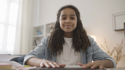 Happy teenage girl having online video call with a friend, smiling at laptop camera