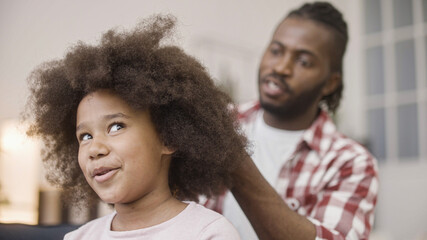 Happy father combing afro hair of little daughter, morning routine, family