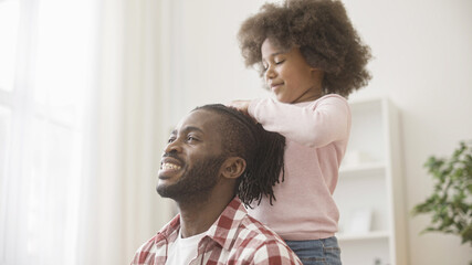 Little girl doing hairstyle for happy dad, black family spending time together