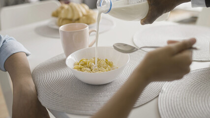 Afro-American father pouring milk into daughter's cereal bowl, family breakfast