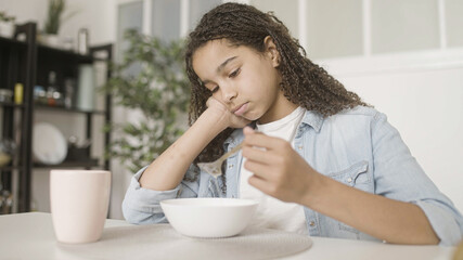 Upset afro-american teenage girl eating cereal, lack of appetite, mood swings