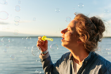 Happy woman is blowing bubbles in front of sea on a warm sunny summer day