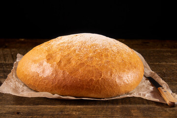 Round hearth bread lying on a wooden table.Bread lying on the paper next to an old knife.
