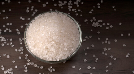 Bowl and spoon with sugar on wooden background.