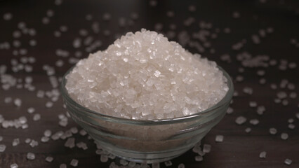 Bowl and spoon with sugar on wooden background.
