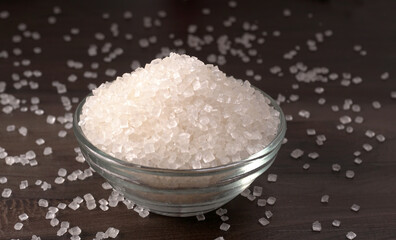 Bowl and spoon with sugar on wooden background.