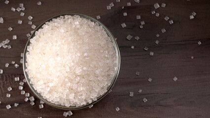 Bowl and spoon with sugar on wooden background.