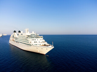 A white passenger cruise ship anchored in calm blue waters in the setting sun.