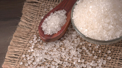 Bowl and spoon with sugar on wooden background.