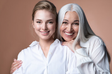 Smiling mature mother and daughter hugging, looking at camera. Middle aged gray-haired mum embracing young beautiful woman shoulders, family photo, two female generations bonding. Mother's Day concept