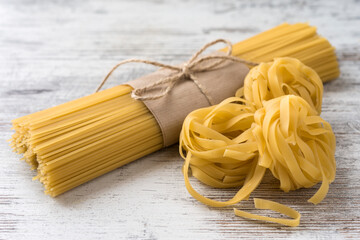 Uncooked spaggetti wrapped in brown paper and tied with twine, fettuccini on a light rustic background