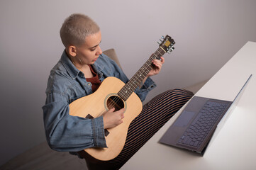 Obraz premium Young caucasian woman with short blonde hair playing guitar and watching training video on laptop.