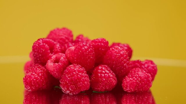 Close-up of rotating ripe red raspberry isolated on yellow background, making jam of fruits and berries, shooting of fresh fruits.