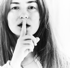 Beautiful young brunette woman puts a finger to her lips. Shh symbol, silence gesture, woman...