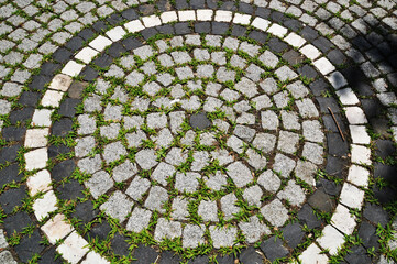 Background, texture. Square cut stones are laid out in a pattern. Circular pattern with stones and green grass.