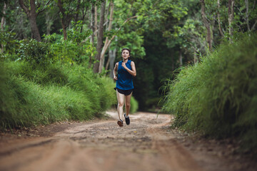 Active Asian woman trail runner running in park outdoor. Trail running athlete through the in the rural road and tropical. Woman running in park.