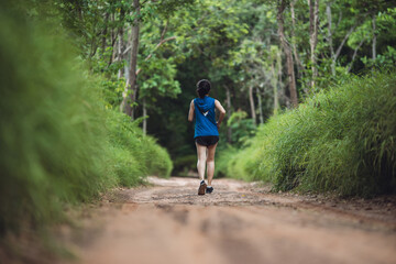 Behind active woman trail runner running in park outdoor. Trail running athlete through the in the rural road and tropical. Woman running in the park.