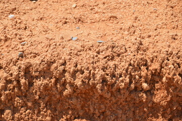 Red and brown sand, dirt and stones texture of a eroded desert beach, with hard sun light