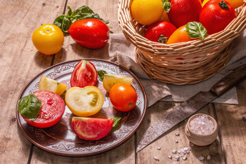 Fototapeta na wymiar Ripe assorted tomatoes with fresh basil in a wicker basket