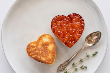Heart shaped pancake and red caviar on gray plate.