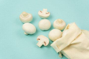 Champignon mushrooms scattered from a fabric bag on a blue background, side view