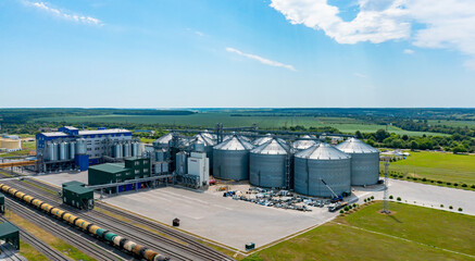 Agricultural industry. Modern factory on green field with steel elevators. Industrial buildings and...