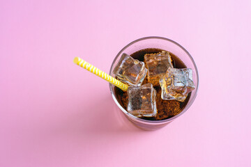 Top view of a glass of cola with ice cubes on pink background