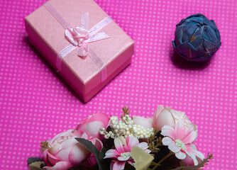 Obraz na płótnie Canvas A flat lay photo of a bouquet of flowers, a gift in the form of a box and accessories on a pink background top view. High quality photo