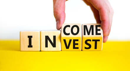 Invest or income symbol. Businessman turns wooden cubes and changes the word 'invest' to 'income'. Beautiful yellow table, white background, copy space. Business and invest or income concept.