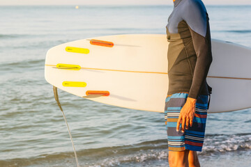 Profile shot of a young man standing with a surfboard on the beach.