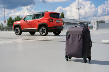 A suitcase in the background of a car in a parking lot. Travel concept
