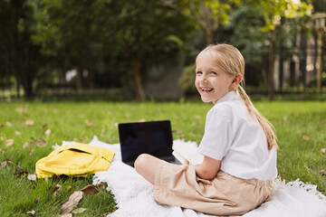 happy caucasian kid has online lesson on laptop during coronavirus covid-19 pandemic and lockdown