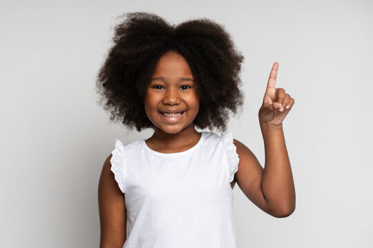 Eureka. Portrait of smart little girl with curly hair pointing finger up and looking inspired by genius thought, showing good idea sign, having clever solution in mind. Studio shot white background
