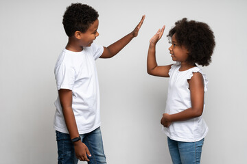 Giving five. Waist up portrait view of the cheerful boy giving five to his sister while posing at the studio with white wall. Family relationships concept