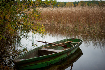 Łódź rybacka na brzegu jeziora czeka na nadejście wiosny. Jesień. Koniec sezonu. - obrazy, fototapety, plakaty