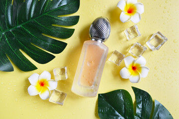 Bottle of perfume with monstera leaves and plumeria flowers on the yellow background. Summer vibes....