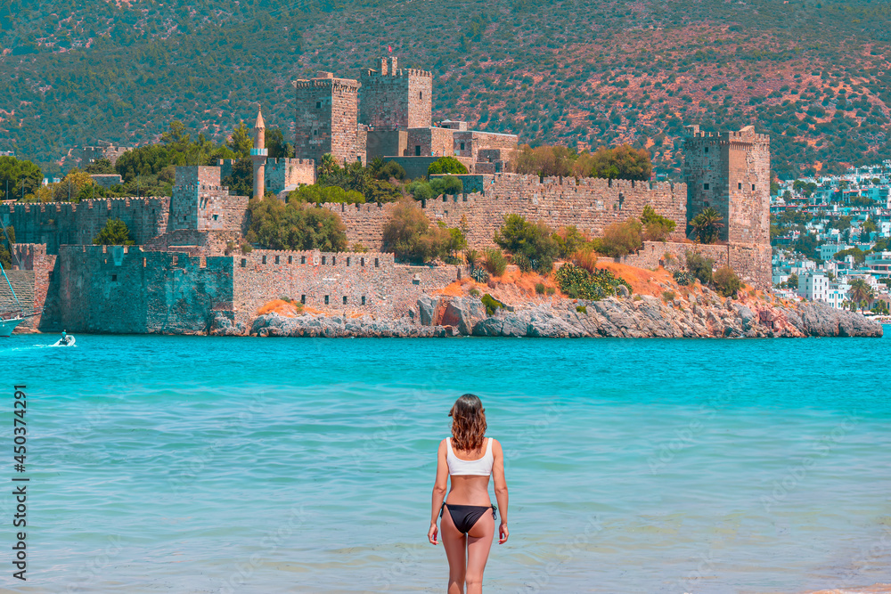 Wall mural beautiful girl in black swimsuit walks on a sandy beach - panoramic view of saint peter castle (bodr