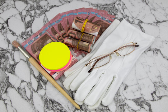 Financial or business concept with a pair of white gloves, eyeglasses and wads and fanned Euro banknotes with colorful circular memo pads over a white marble background in a flat lay view